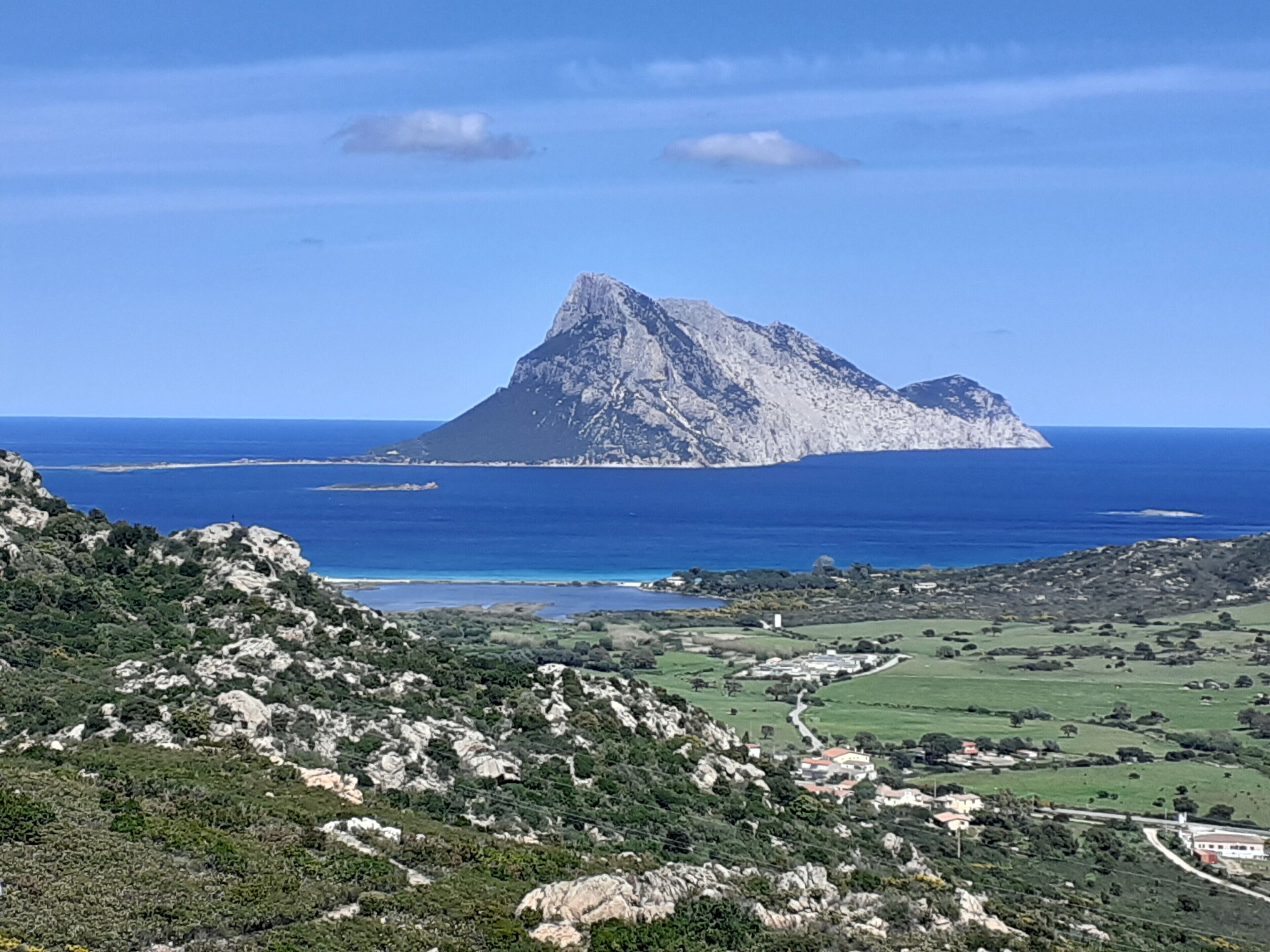 Eine gebirgige Landschaft mit einem markanten Gipfel, Blick auf die Küste und einem Tal mit verstreuten Gebäuden.