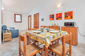 A dining area with a table set for four, surrounded by wooden chairs, a blue sofa, and a wicker side table. - Apartment 'Il Glicine' close to the Sea with Terrace & A/C (vaccileddi)
