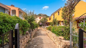 A narrow stone pathway flanked by buildings with balconies and a stone wall.