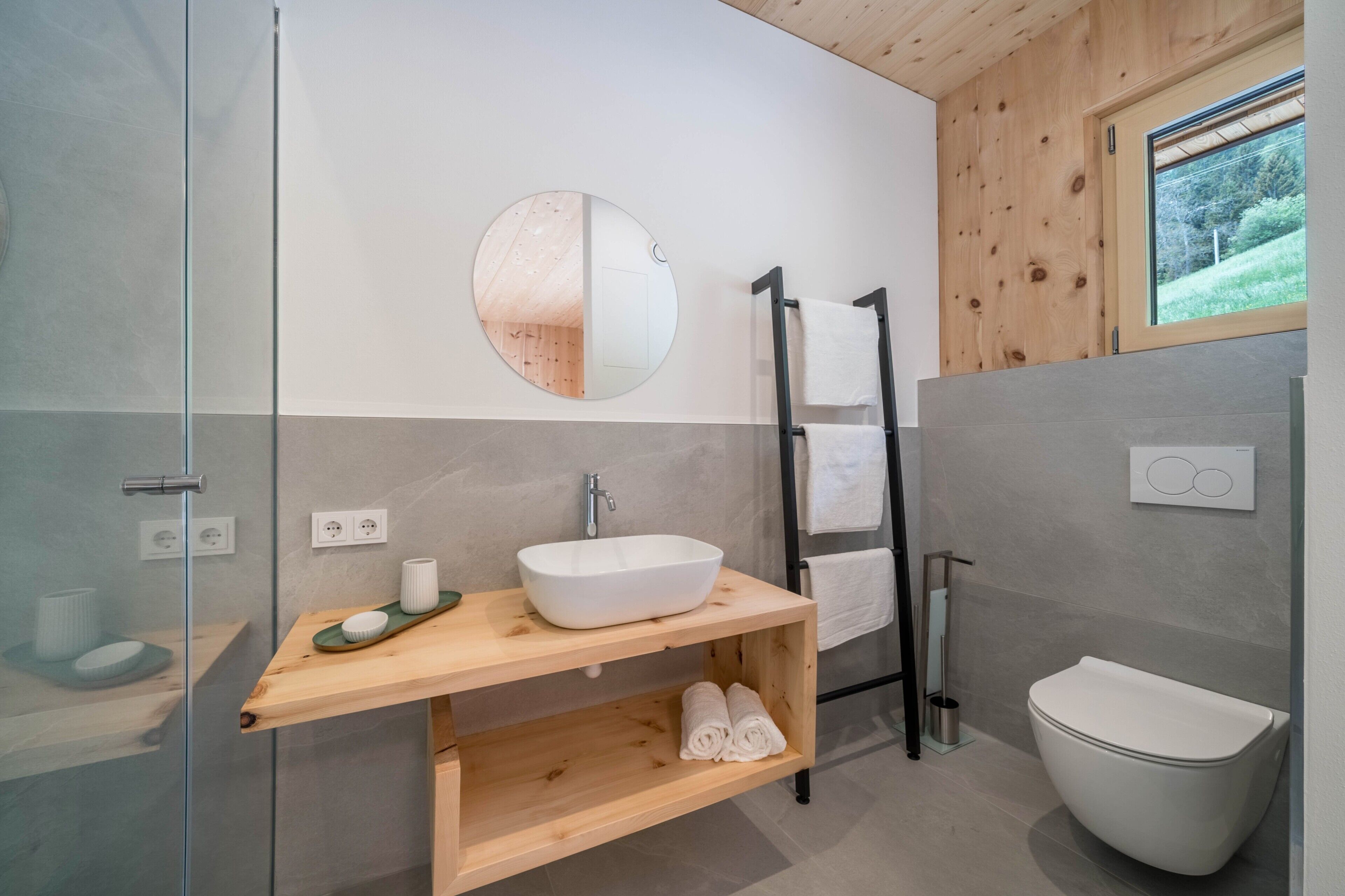 Une salle de bain moderne avec une douche à parois de verre, un meuble-lavabo en bois, un porte-serviettes et des toilettes.