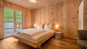 Habitación de madera con cama, dos lámparas de noche y vistas a través de un ventanal.