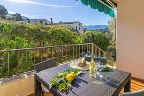 Un balcon agrémenté de meubles en osier, une table avec une bouteille et des verres, et une vue sur la verdure et les bâtiments.