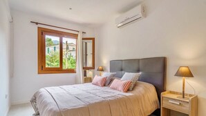 A bedroom with a bed, bedside tables, a window with curtains, and an air conditioning unit. - Holiday Home "Yolima" near the Beach with Wi-Fi, Air Conditioning and Garden (Sóller)