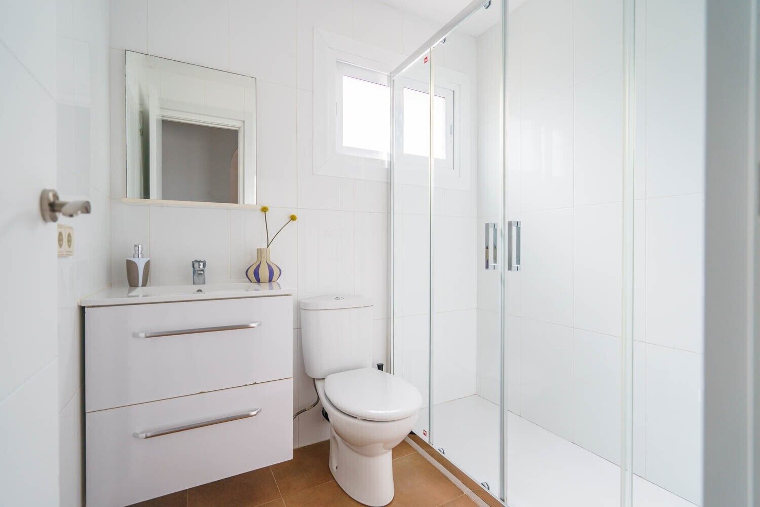 Un bagno moderno con un mobile lavabo bianco, il water e cabina doccia in vetro.