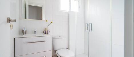 Un bagno moderno con un mobile lavabo bianco, il water e cabina doccia in vetro.