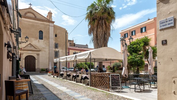 A street with outdoor seating, a church, and a palm tree. - Apartment "Dimora Teatro" with Landmark View & A/C (Alghero)