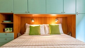 A bed with a quilted bedspread, two pillows, a wooden headboard with built-in lighting, and a green cabinet with a shelf. - Apartment "Dimora Teatro" with Landmark View & A/C (Alghero)