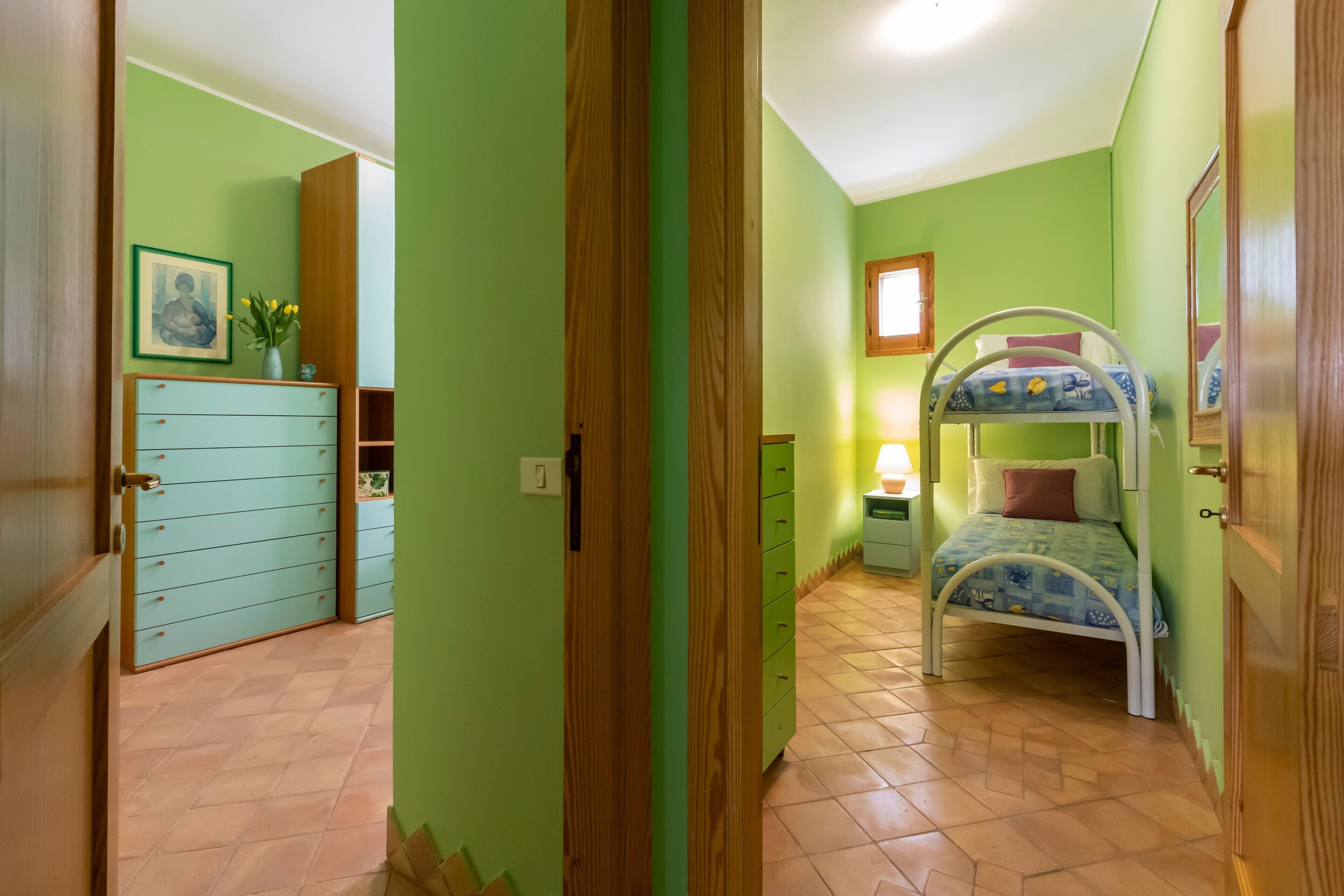 Ein Zimmer mit einem Etagenbett, einem Schminktisch, einem kleinen Tisch mit Lampe und einem gerahmten Bild an der Wand.