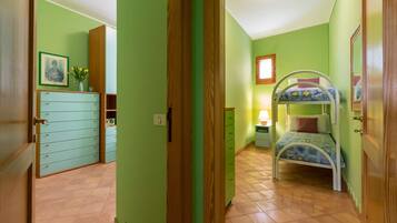 Ein Zimmer mit einem Etagenbett, einem Schminktisch, einem kleinen Tisch mit Lampe und einem gerahmten Bild an der Wand.