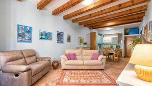 A living room with a beige sofa, a patterned rug, and wooden beams on the ceiling. - Apartment "Dimora Teatro" with Landmark View & A/C (Alghero)