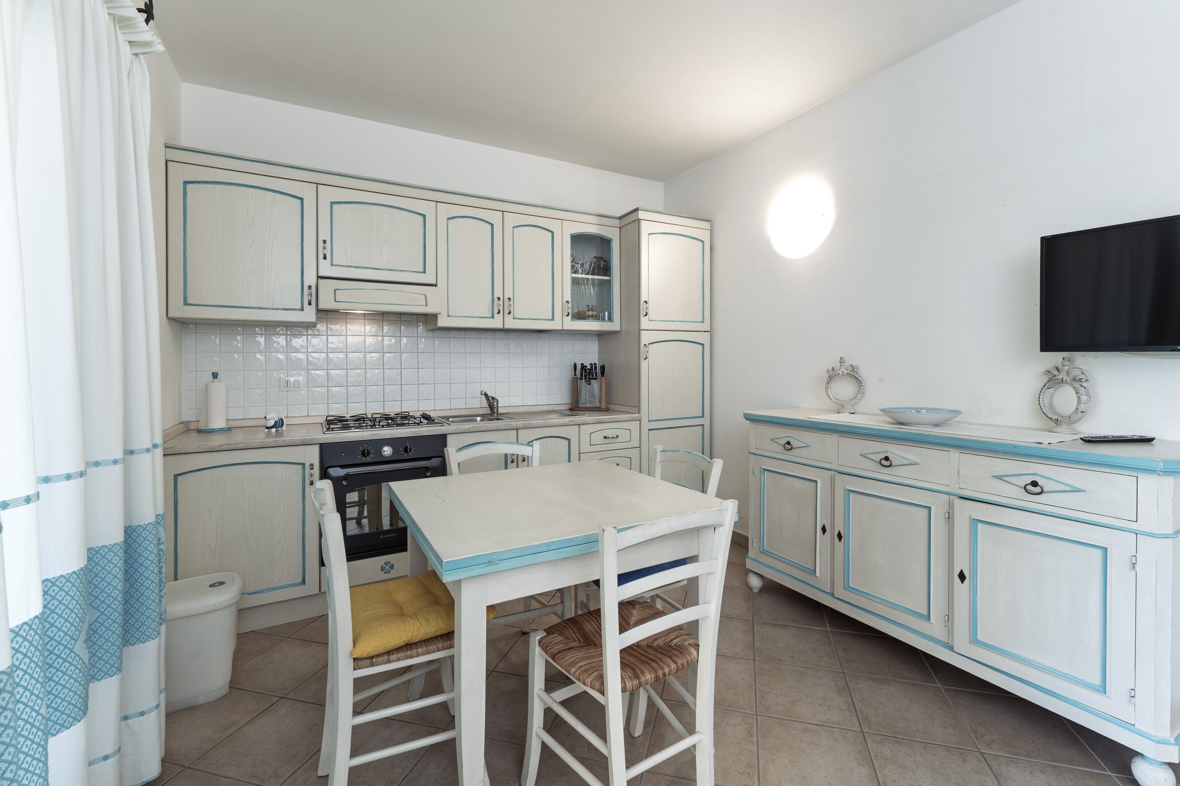 A kitchen with white cabinets, a stove, a sink, and a dining table with chairs.