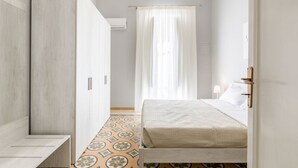 Un dormitorio con cama, armario, ventana con cortinas y suelo estampado.