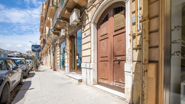 Una calle con coches aparcados, un edificio con un gran puerta de madera y un cartel sobre la puerta.