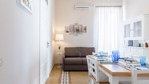 Un espacio habitable compacto con sofá, mesa de comedor y una pequeña mesita de noche con lámpara.