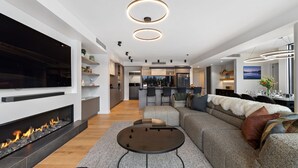 A modern living room with a fireplace, a large TV, a sofa, and a dining area with a view of the kitchen.