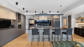 A modern kitchen with a central island, bar stools, a refrigerator, and a view of the outdoors.
