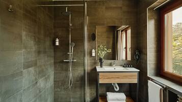 Un baño moderno con ducha de vidrio, tocador de madera y un ventanal grande.