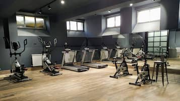 Uma academia com vários equipamentos de ginástica, grandes janelas e piso de madeira.