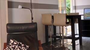 Una sala de estar moderna con un sofá de cuero negro, una lámpara de pie y un comedor con taburetes de bar.