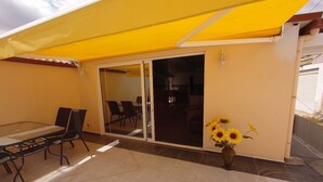 Un patio con una mesa, sillas, un cerramiento de vidrio corredero y un toldo amarillo.