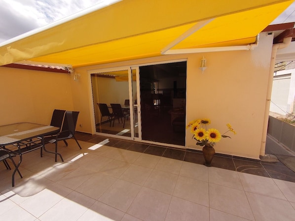 A patio with a table and chairs, a sliding glass door, and a yellow awning. - Vacation apartment Marlene (El Salobre)