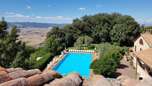 Piscina rectangular con sillas de descanso y sombrillas, rodeada de árboles y vistas a colinas distantes.