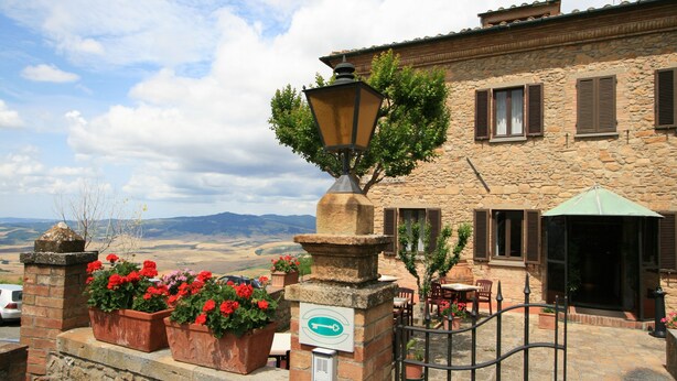 Un edificio de piedra con patio, mesas al aire libre y jardineras con flores.