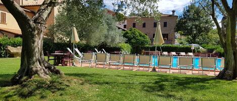 A pool area with lounge chairs and umbrellas, surrounded by trees and buildings.