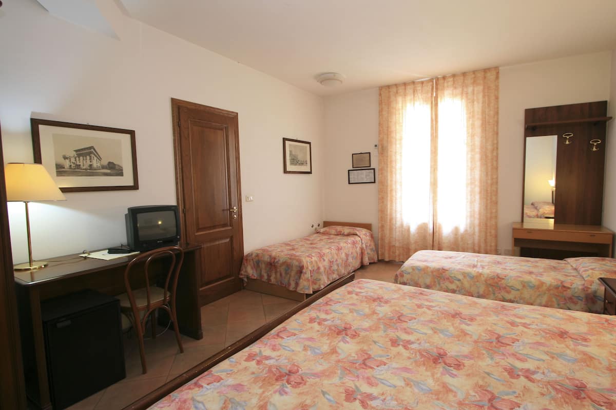 A hotel room with two single beds, a desk with a computer, a chair, a small refrigerator, and a mirror.