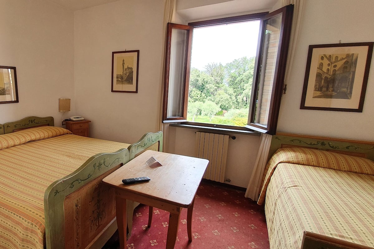 A hotel room with two single beds, a wooden table with a remote control, a nightstand, and framed pictures on the walls.