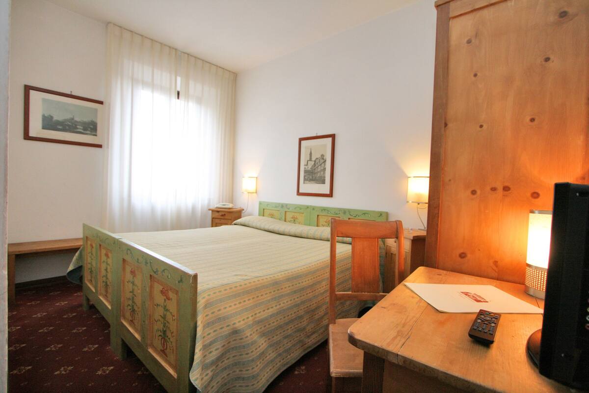 A hotel room with a bed, a desk with a lamp, a chair, and a television.