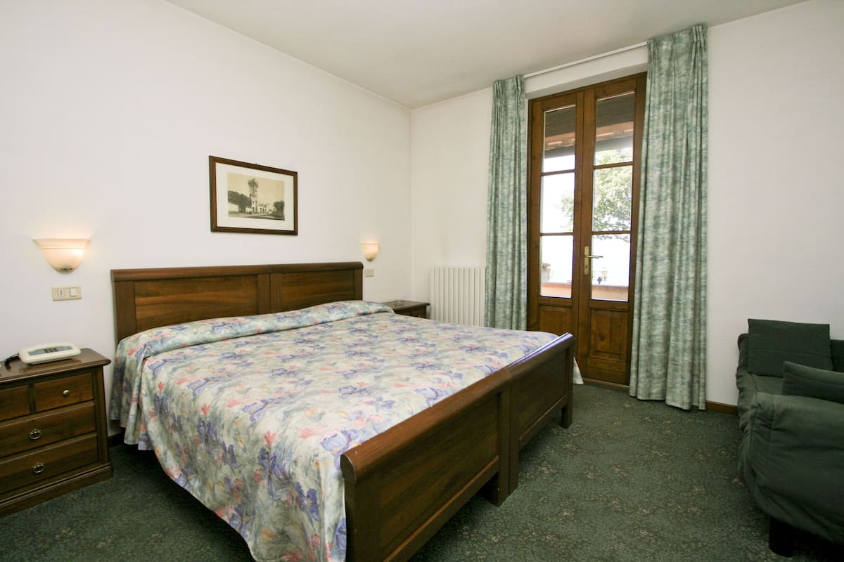 A bedroom with a wooden bed, two bedside tables, a nightstand, a framed picture on the wall, and a window with curtains.