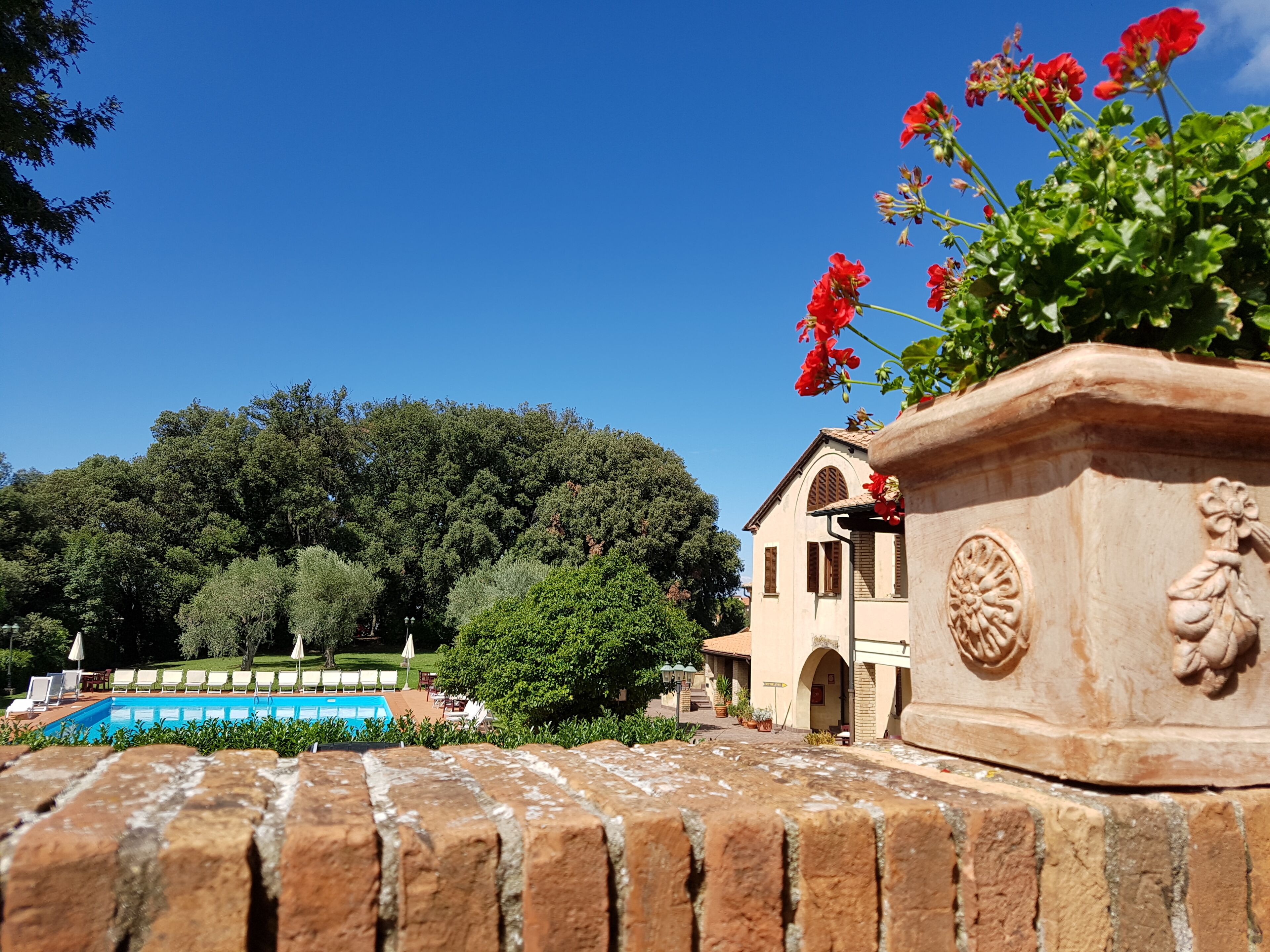 A pool area with a clear blue sky, a brick wall, and a building with a tiled roof.