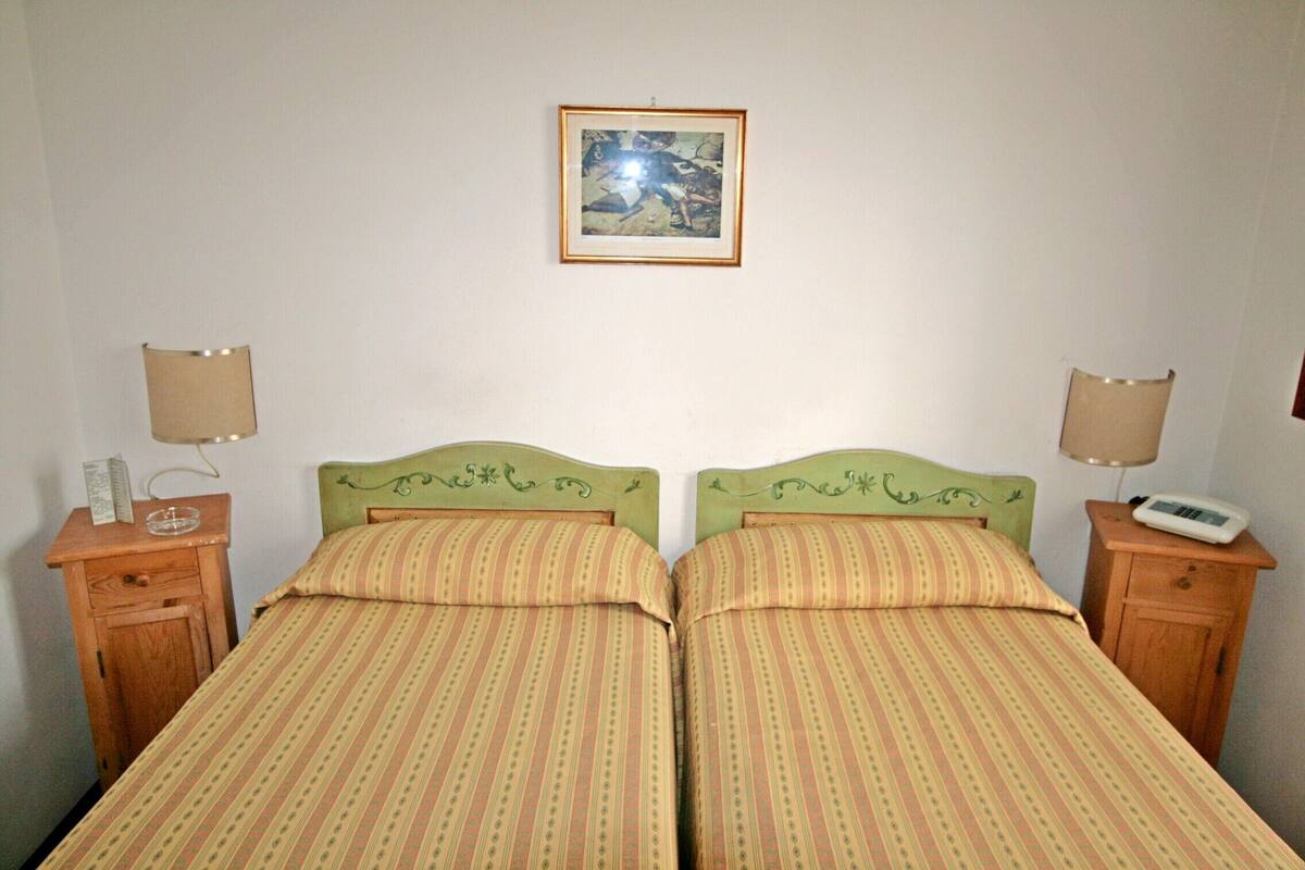 A double bed with striped bedding, two bedside tables with lamps, and a framed picture on the wall.