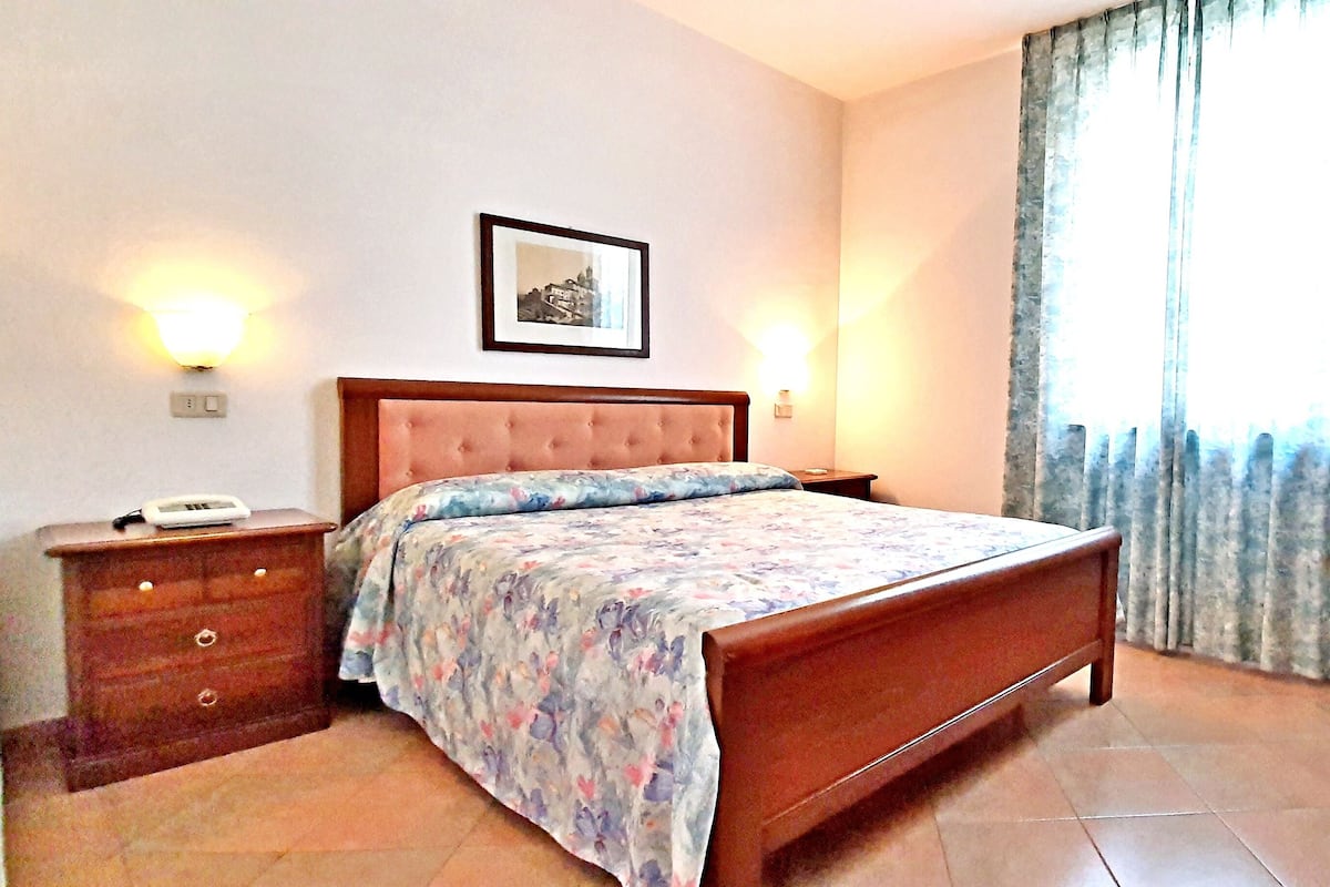 A bedroom with a bed, dresser, bedside lamps, a framed picture, and a window with curtains.