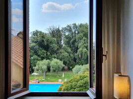 Vista a través de una ventana que muestra una piscina rodeada de exuberante vegetación y árboles.