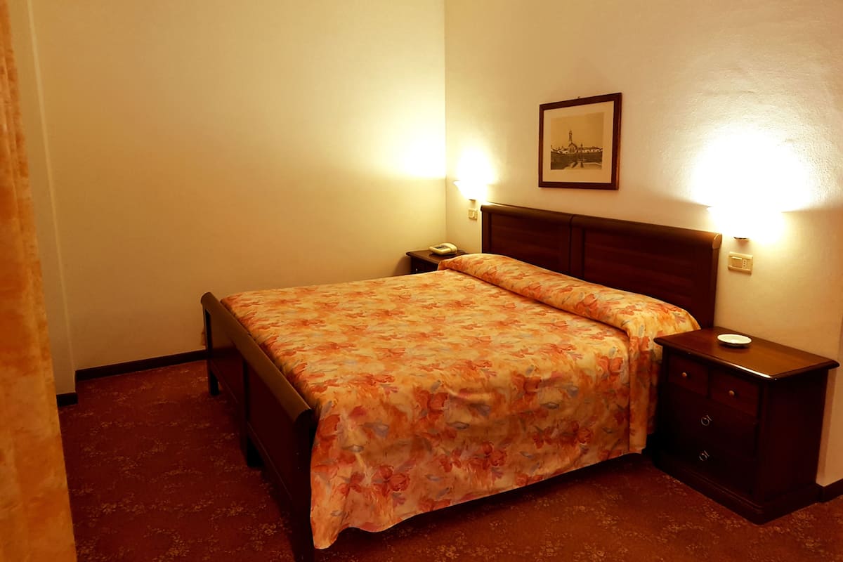 A hotel room with a bed, nightstands, a framed picture on the wall, and two wall-mounted lamps.