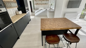 A modern kitchen with dark cabinetry, a wooden countertop, and a central island with stools. - Island House is a spacious 4 bedroom detached house (West Mersea)