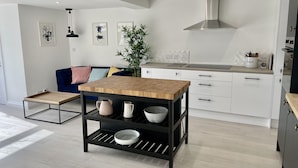 A modern kitchen with white cabinets, a wooden table, and a black shelf unit. - Island House is a spacious 4 bedroom detached house (West Mersea)