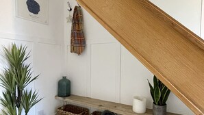 A staircase with a wooden handrail, a potted plant, a shelf with baskets, and a wall with framed artwork. - Island House is a spacious 4 bedroom detached house (West Mersea)