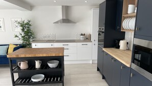 A modern kitchen with a wooden table, black shelves, and a built-in oven. - Island House is a spacious 4 bedroom detached house (West Mersea)