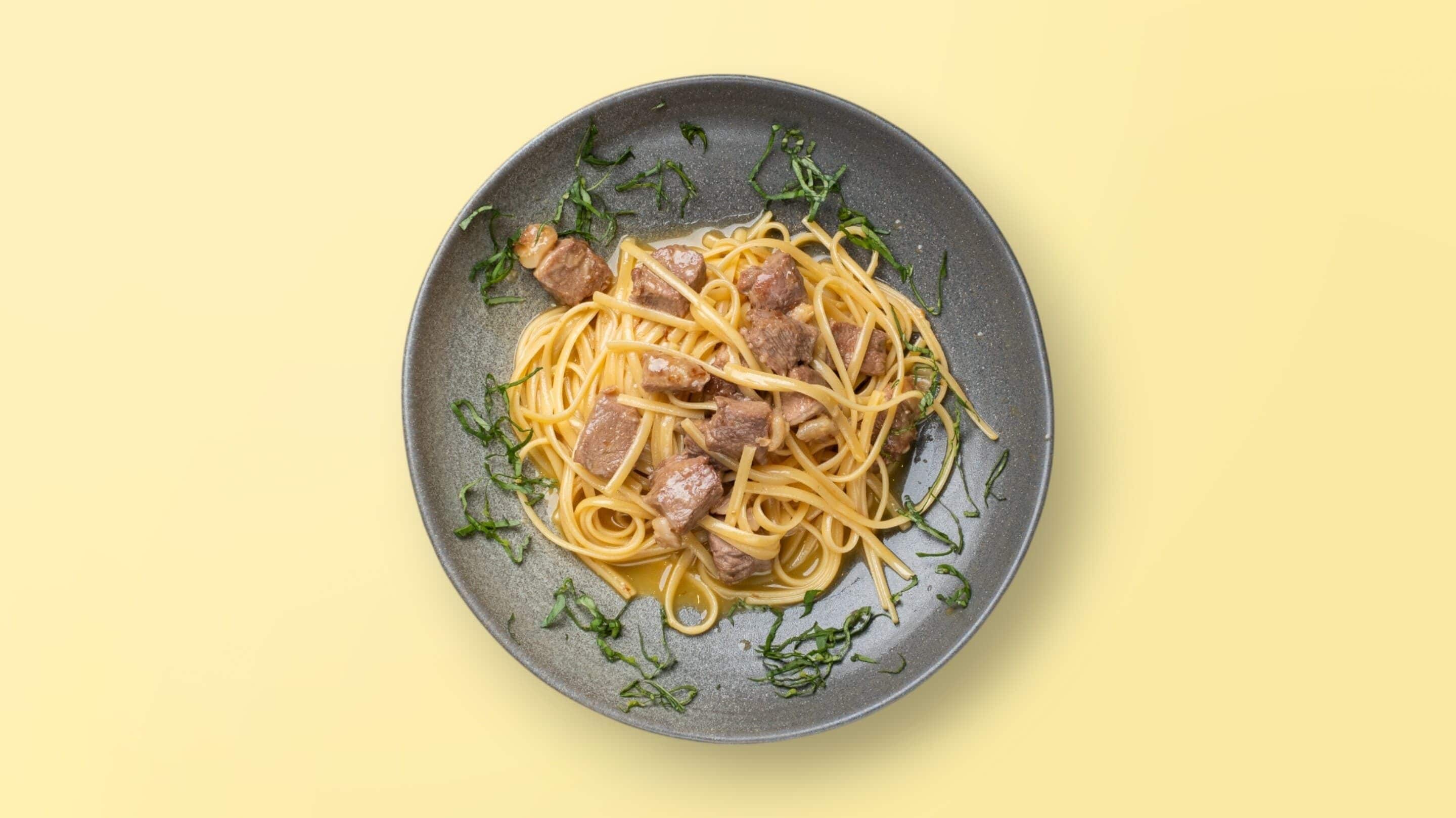 A plate of spaghetti with meatballs and garnished with herbs.