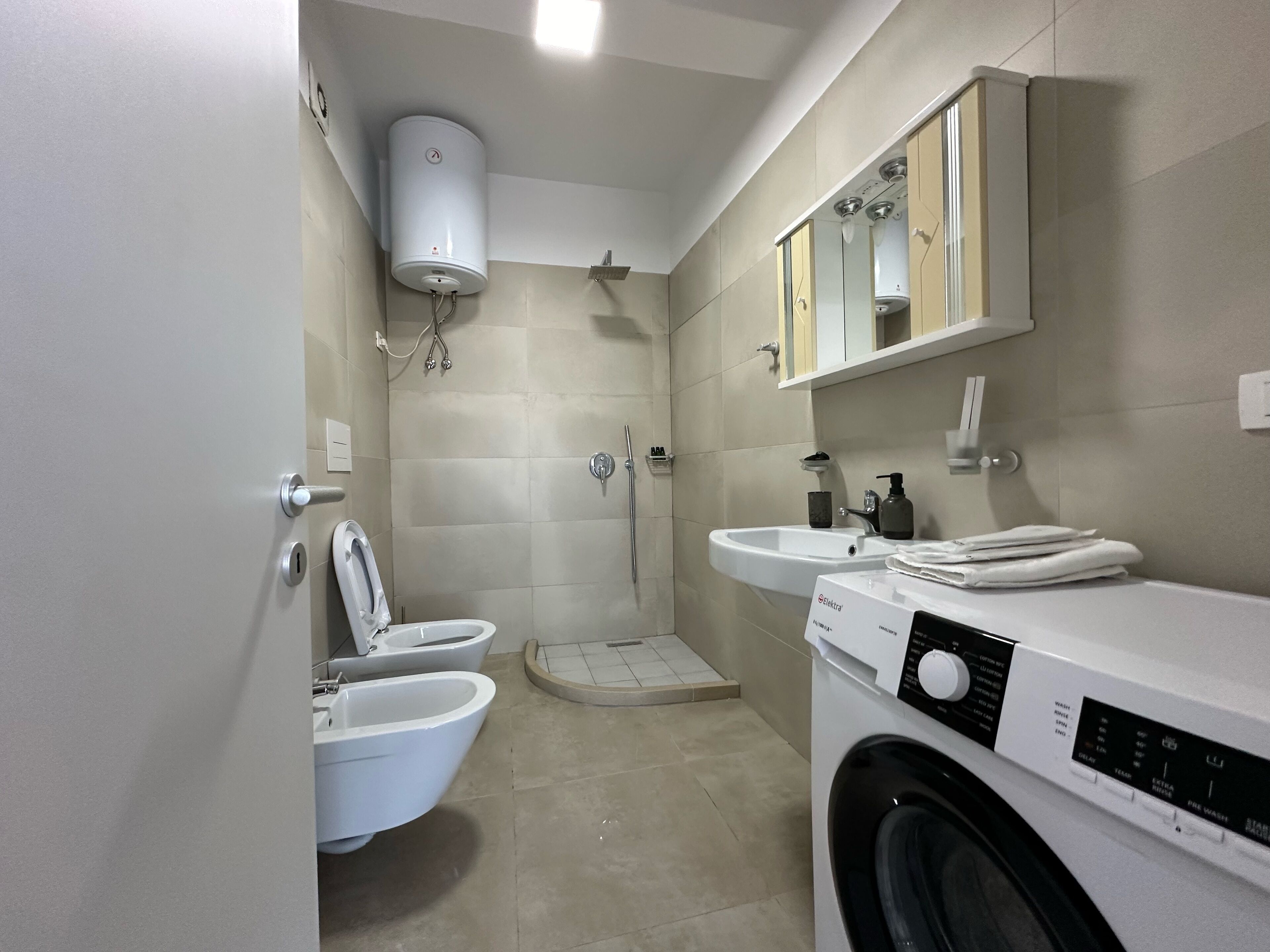 A modern bathroom with a toilet, bidet, shower, sink, and a washing machine.
