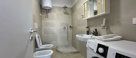 A modern bathroom with a toilet, bidet, shower, sink, and a washing machine.