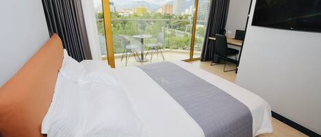 A hotel room with a large bed, a balcony with a table and chairs, and a TV on the wall.