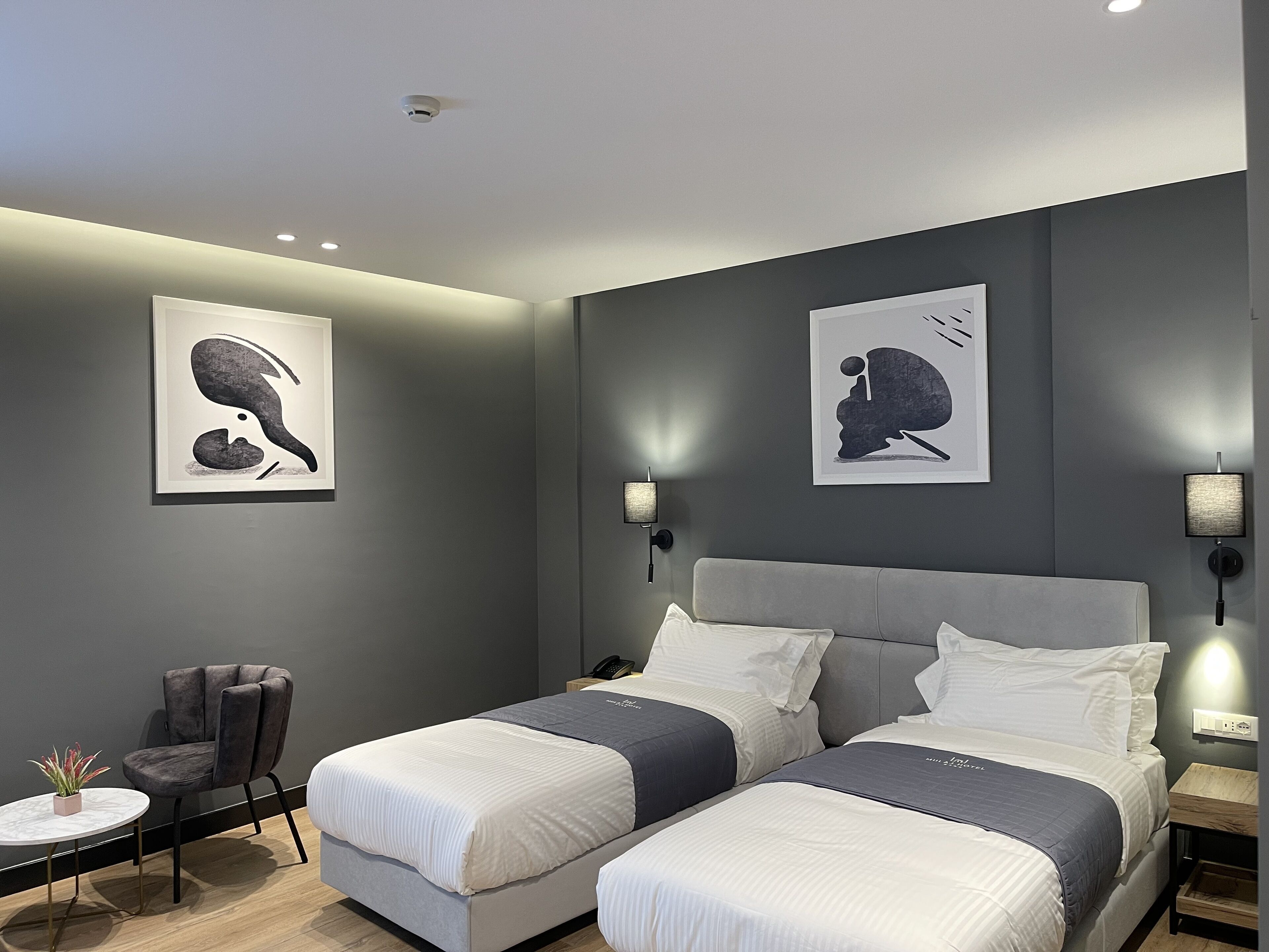 Un dormitorio moderno con dos camas, una silla, una mesita y lámparas de pared.