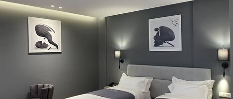 Un dormitorio moderno con dos camas, una silla, una mesita y lámparas de pared.