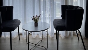 Una habitación moderna con vista al agua, que incluye dos sillas negras, una mesita y cortinas traslúcidas.