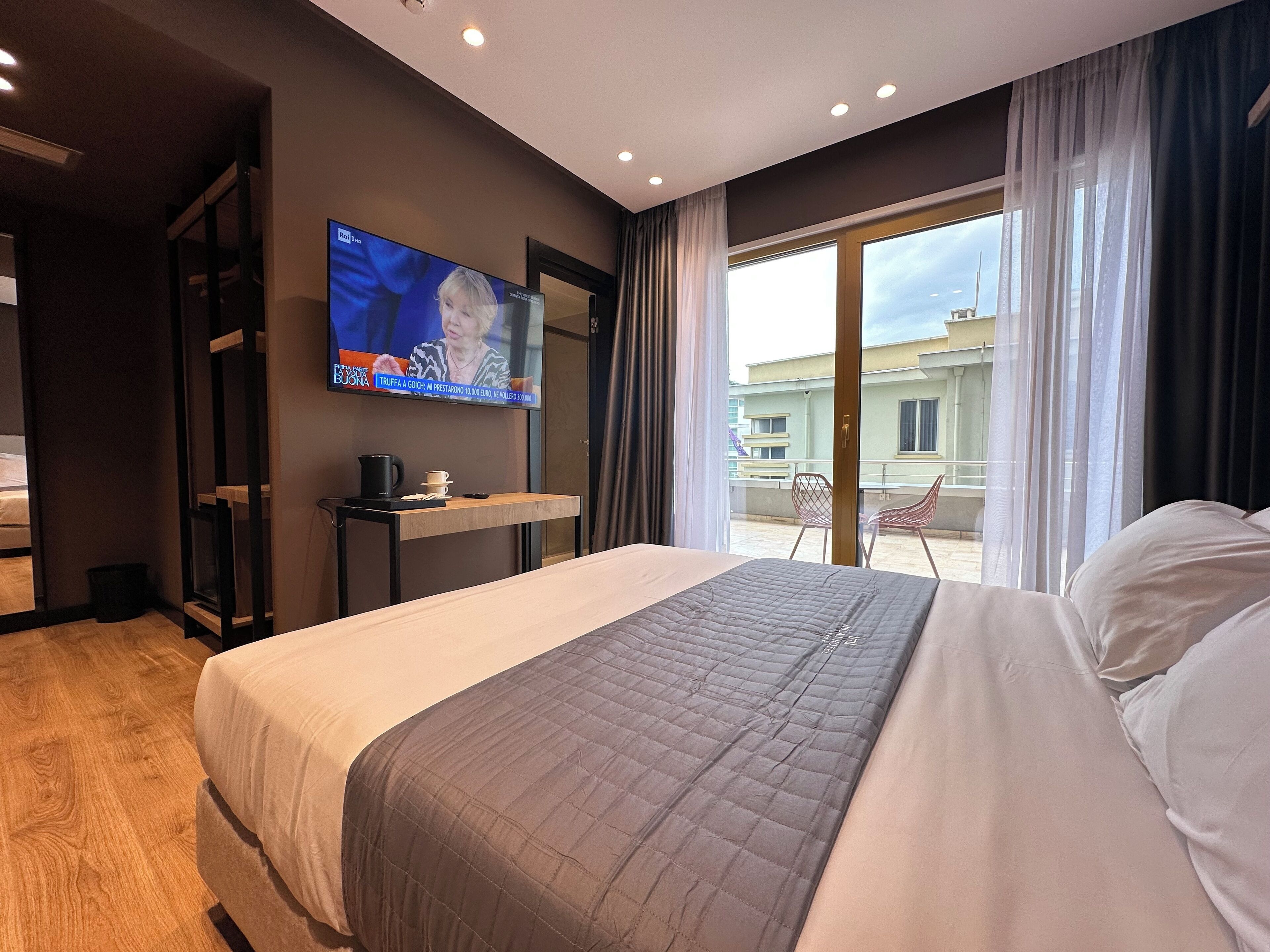 Une chambre d’hôtel avec un grand lit, un téléviseur fixé au mur, une petite table avec une cafetière et une vue sur le balcon extérieur.