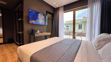 Une chambre d’hôtel avec un grand lit, un téléviseur fixé au mur, une petite table avec une cafetière et une vue sur le balcon extérieur.